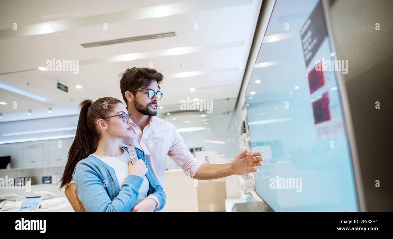 Gioiosa giovane attraente coppia multirazziale che controlla le TV al plasma nel negozio elettronico. Foto Stock