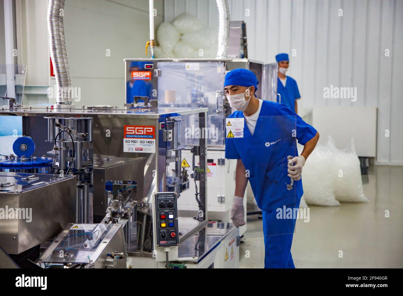 Atyrau, Kazakistan. Impianto di produzione di siringhe mediche. Giovane operatore asiatico sulla linea di produzione. Foto Stock