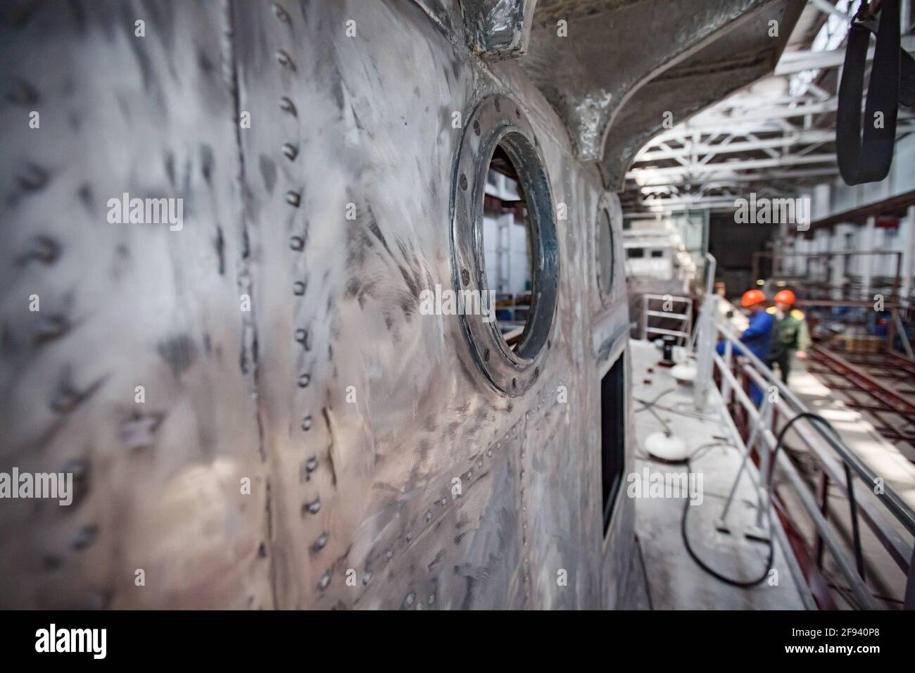 Impianto di costruzione di navi. Pozzetto in metallo graffiato e non verniciato con illuminatore a foro di vetro. Lavoratori blured sullo sfondo. Foto Stock