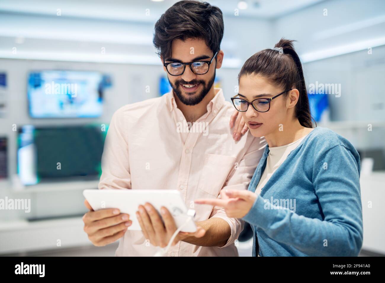 Coppia multiculturale che testa il nuovo modello di un tablet nel negozio di tecnologia. Clienti che acquistano un nuovo tablet. Foto Stock