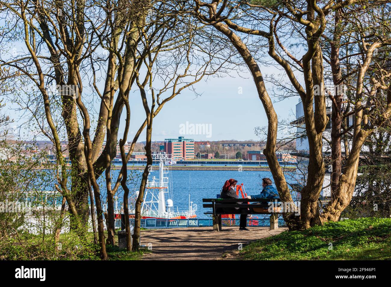 Kiel Botanischer Garten im Frühjahr. Ein Mann und eine Frau genießen den Frühling auf einer Bank mit Blick auf den Kieler Hafen Foto Stock