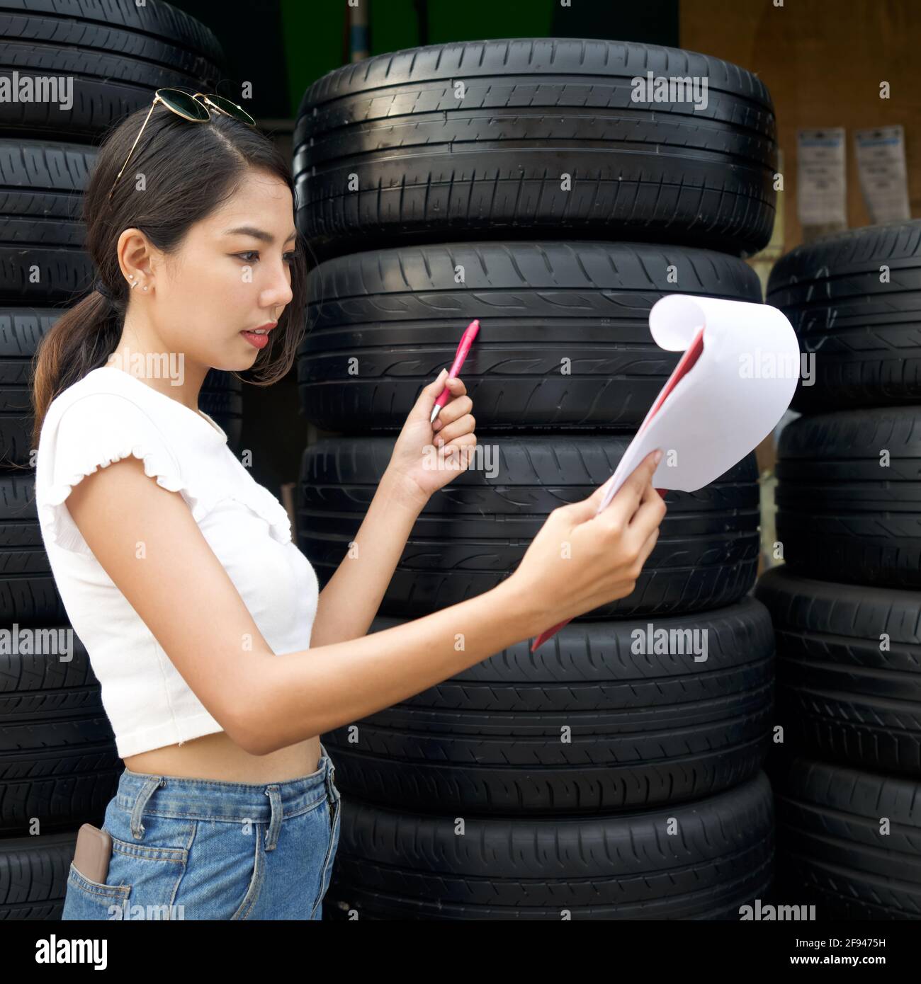 Il giovane proprietario asiatico del negozio di ricambi auto controlla il numero di pneumatici e gli ordini in arrivo prima di iniziare il lavoro al mattino. Diversi pneumatici per auto ar Foto Stock