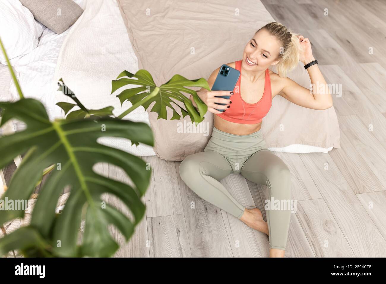 Bella istruttore di yoga femminile utilizzando smartphone, facendo l'allenamento online da casa, sorridendo. Felice giovane donna in elegante sportswear che fa un selfie Foto Stock