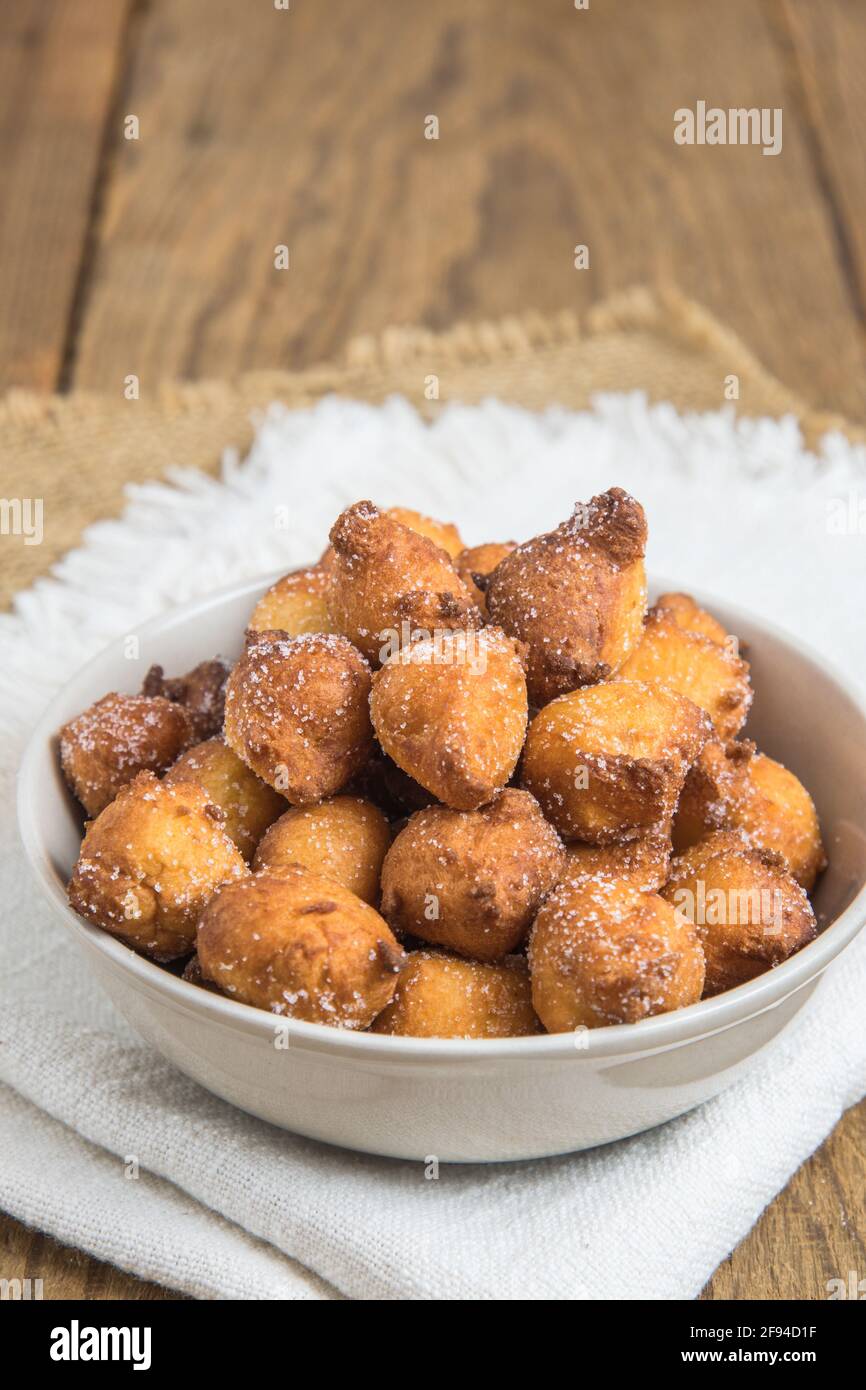 Mutzen o Castagnole fatti in casa, frittelle di carnevale tipiche tedesche o italiane con zucchero in una ciotola bianca su rustico tavolo di legno, verticale con spazio per la copia Foto Stock