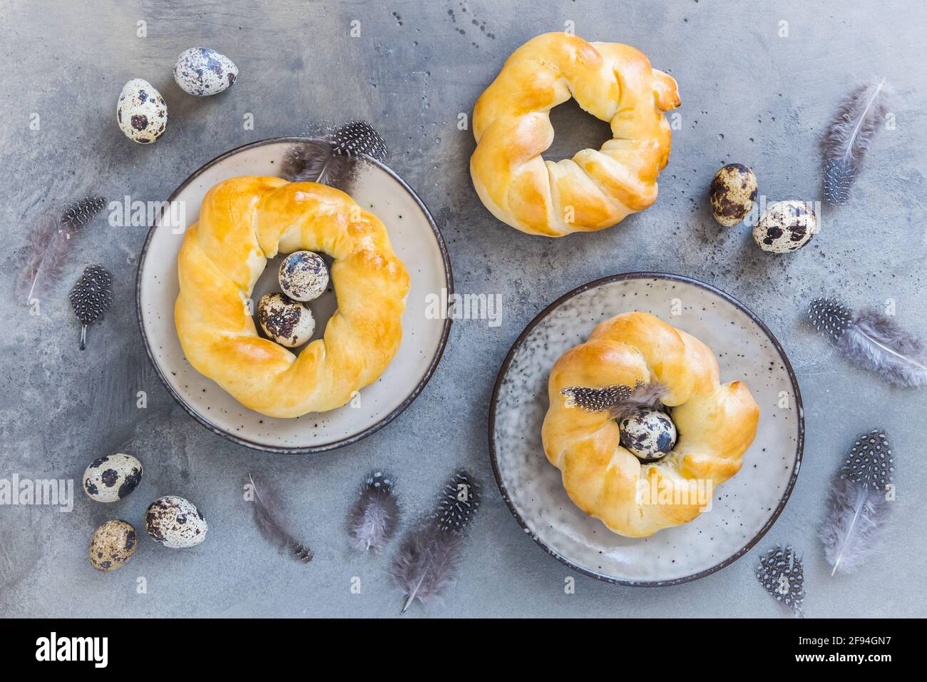 Focaccine pasquali fatte in casa su sfondo grigio, decorate con uova naturali e piume, vista dall'alto Foto Stock