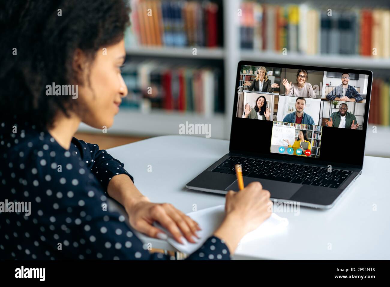 Formazione online tramite videoconferenza. La studentessa afroamericana prende appunti durante una lezione, su un computer portatile schermo femmina insegnante conduce una lezione online per gli studenti. Concetto di comunicazione virtuale Foto Stock