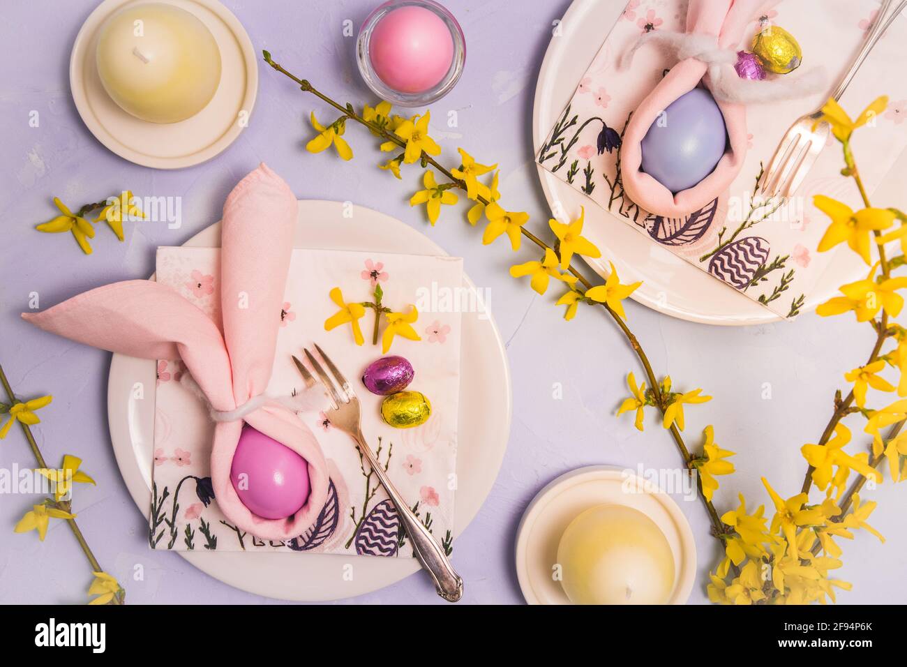 Tavola pasquale decorata con tovaglioli e uova come coniglietto pasquale, candele d'uovo e rami di forsizia fresca, vista dall'alto Foto Stock