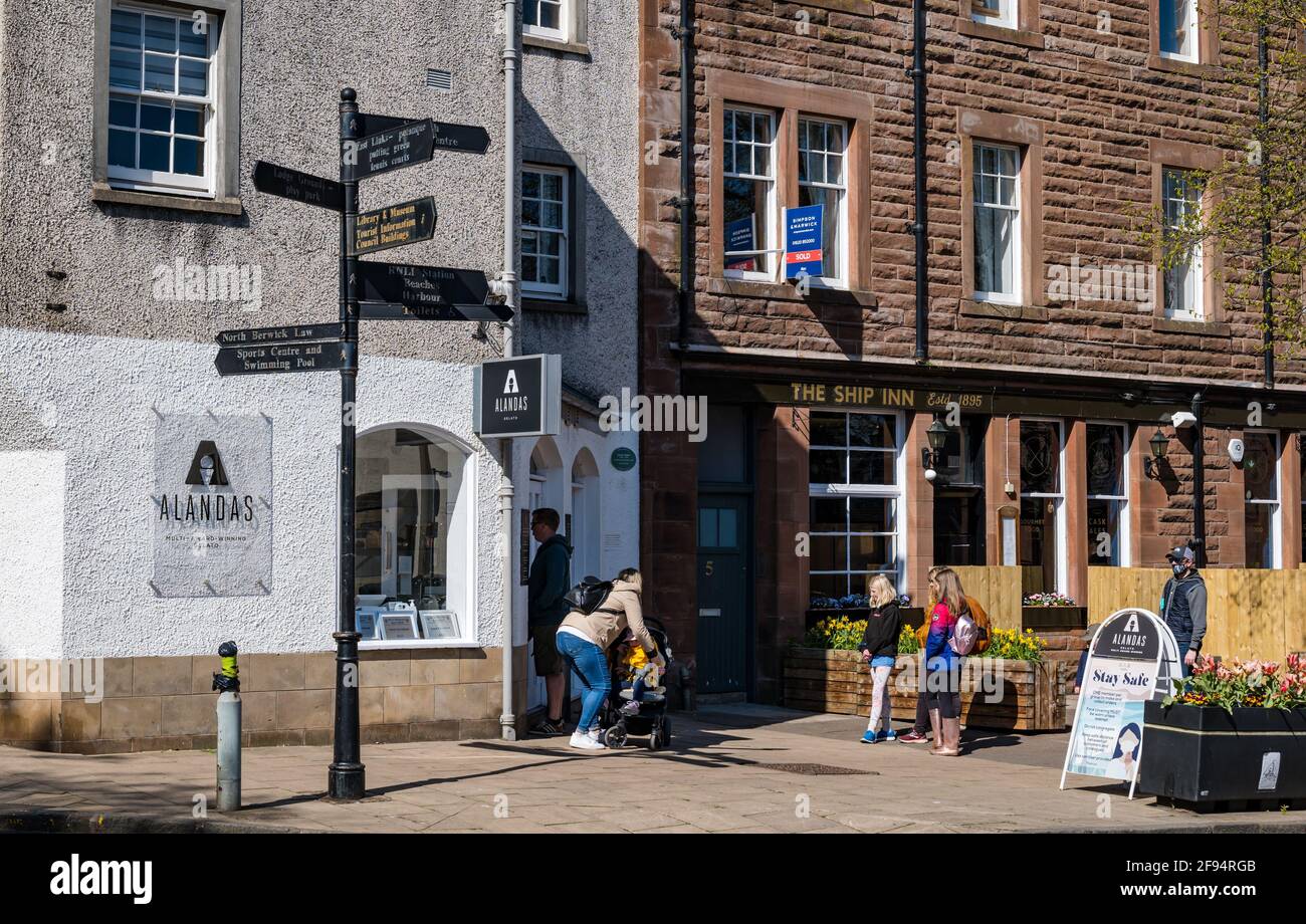 North Berwick, East Lothian, Scozia, Regno Unito. 16 Apr 2021. Le persone si dirigono verso il mare dopo che le restrizioni di viaggio sono sollevate: Il sole è fuori, il tempo è più caldo e la gente può ancora una volta godere di un viaggio alla città costiera. Nella foto: Una coda di persone aspetta fuori dalla premiata gelateria Alandas Foto Stock