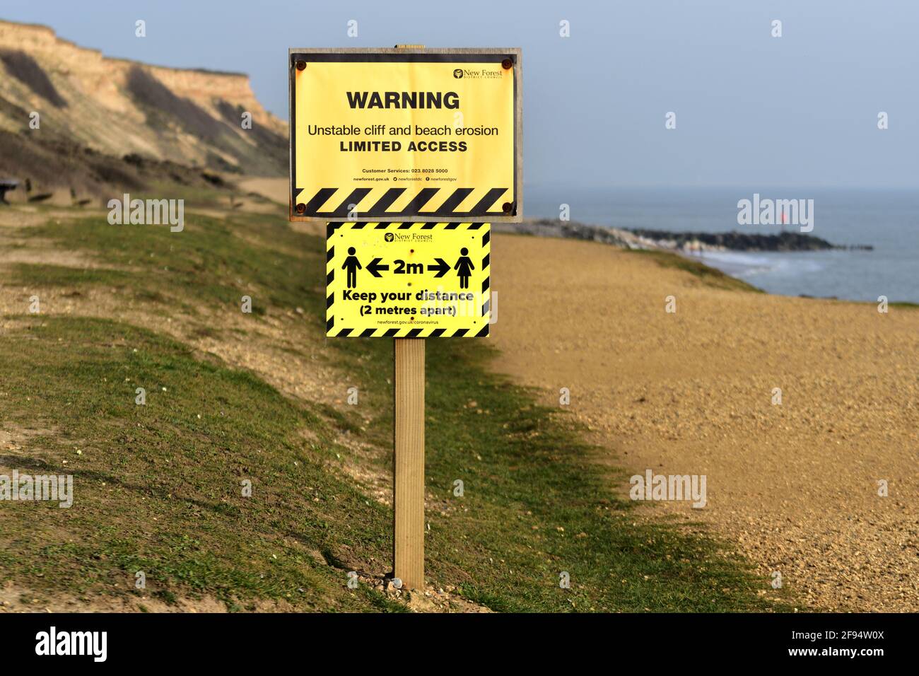 Due preoccupazioni attuali in una: Erosione costiera e allontanamento sociale. . Barton-on-Sea, New Forest, Hampshire, Inghilterra. Foto Stock