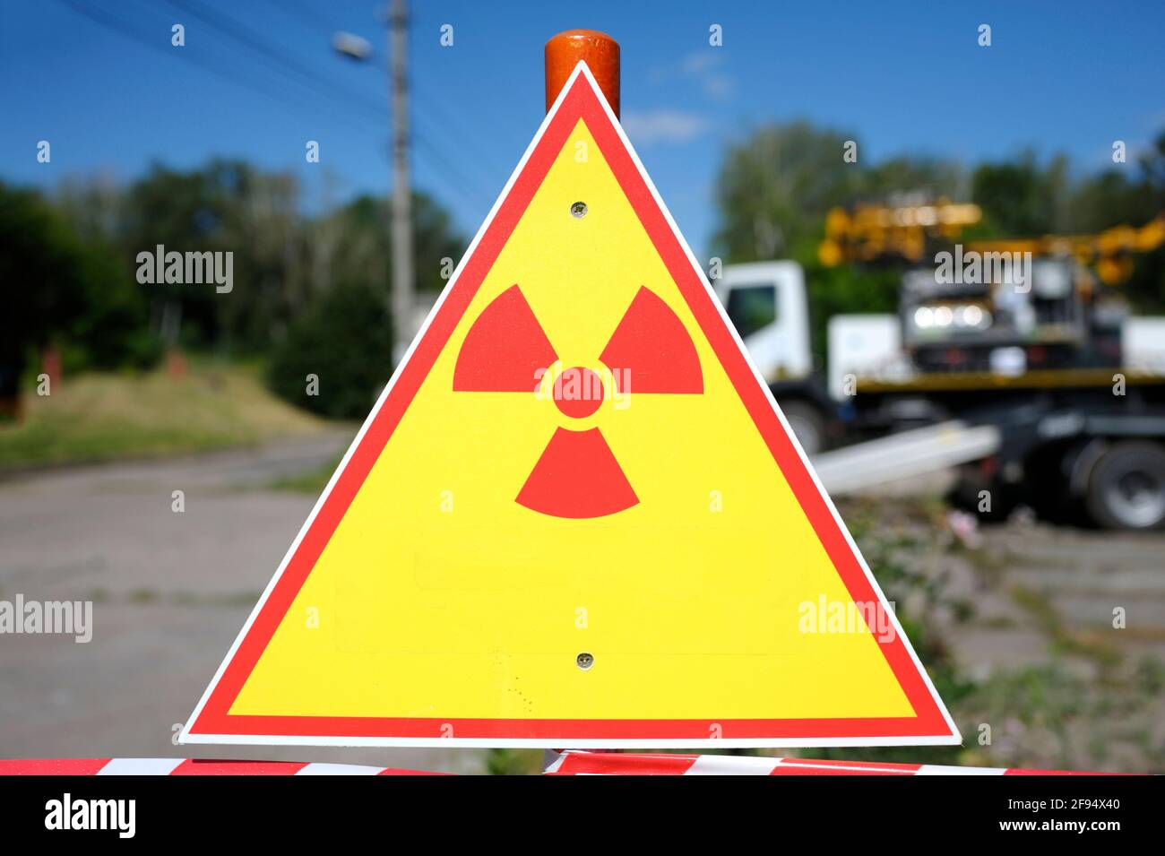 Segnale di pericolo di radiazioni, alberi e camion sullo sfondo. Foto Stock