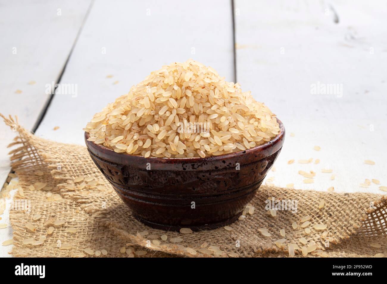 Riso Kerala Matta  riso parboiled o palakadan matta o rosso riso disposto in una ciotola di legno che è messo sopra un panno di iuta con sfondo bianco Foto Stock