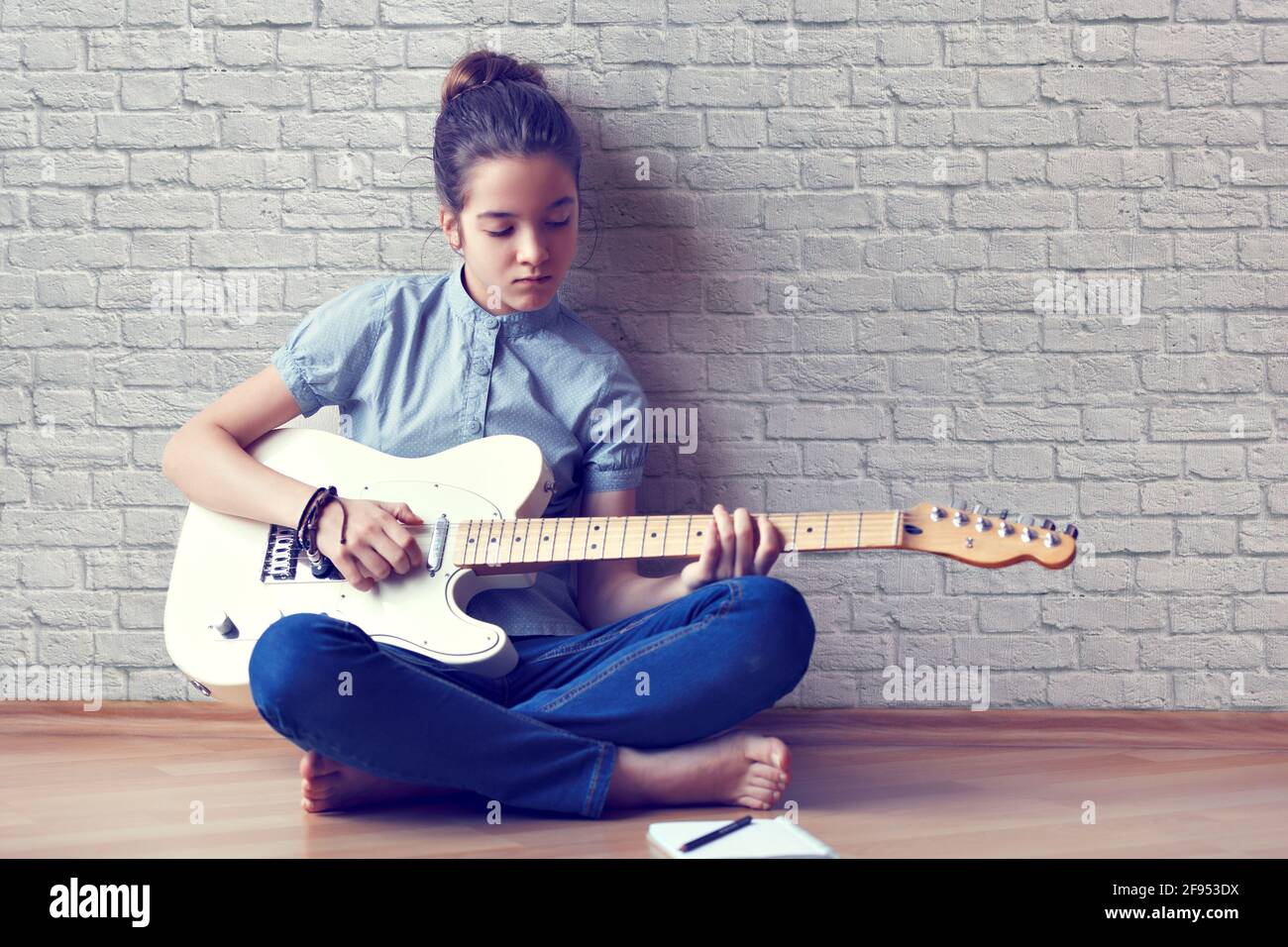 Bella giovane ragazza suona la chitarra e compone la musica su uno sfondo di un muro di mattoni., bella giovane ragazza suona la chitarra e compone la musica su un backg Foto Stock