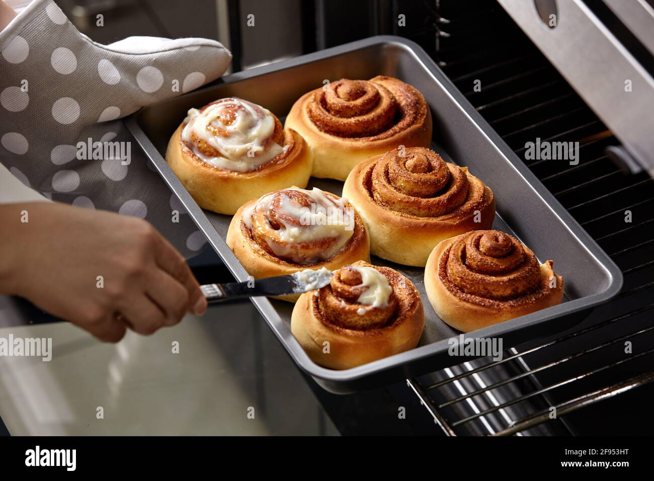 La donna ha strisciato le ciambelle rifinite con la crema. I panini alla cannella vengono cotti nel forno. Cottura fatta in casa. Foto Stock