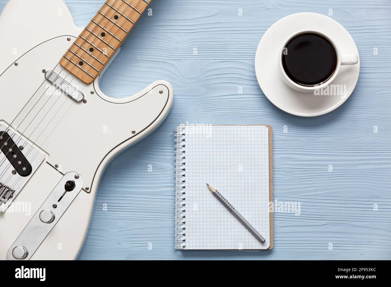 Una tazza di caffè, una chitarra e un taccuino su una tavola di legno chiaro. Foto Stock