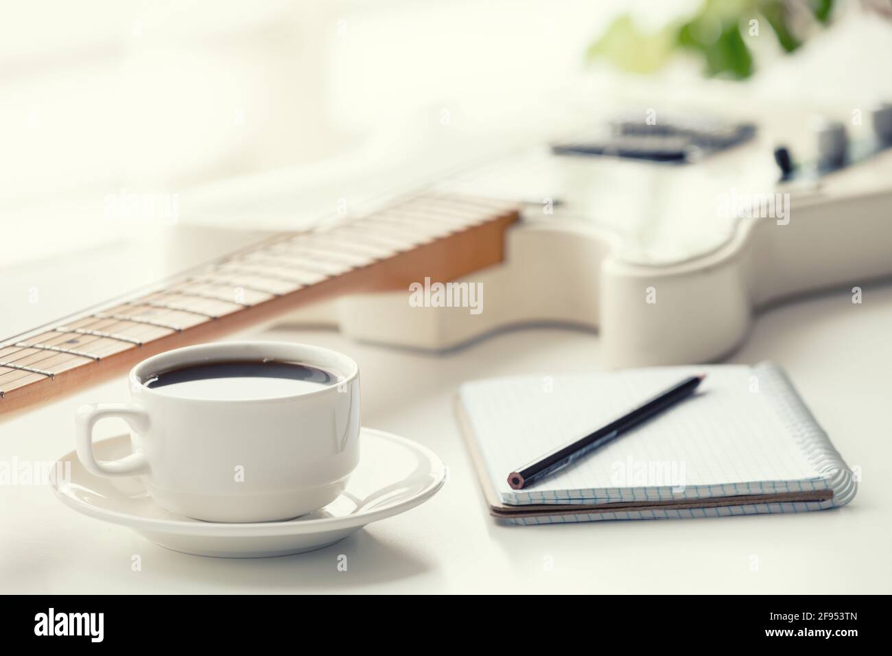 Chitarra, caffè, blocco note e matita su sfondo chiaro. Foto Stock