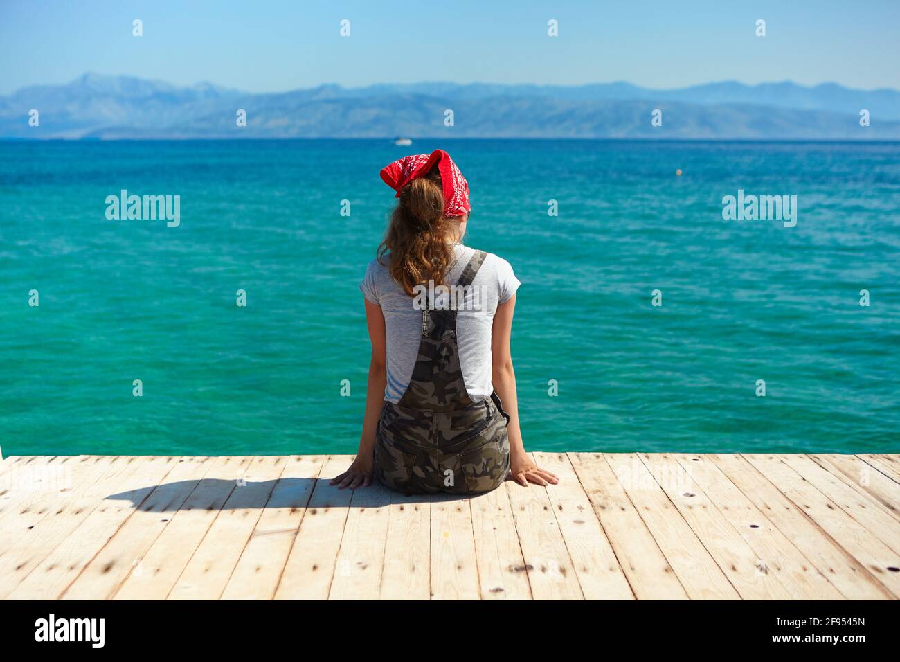 Una giovane ragazza si siede su un molo di legno e guarda al mare. Stile di vita sano. Foto Stock