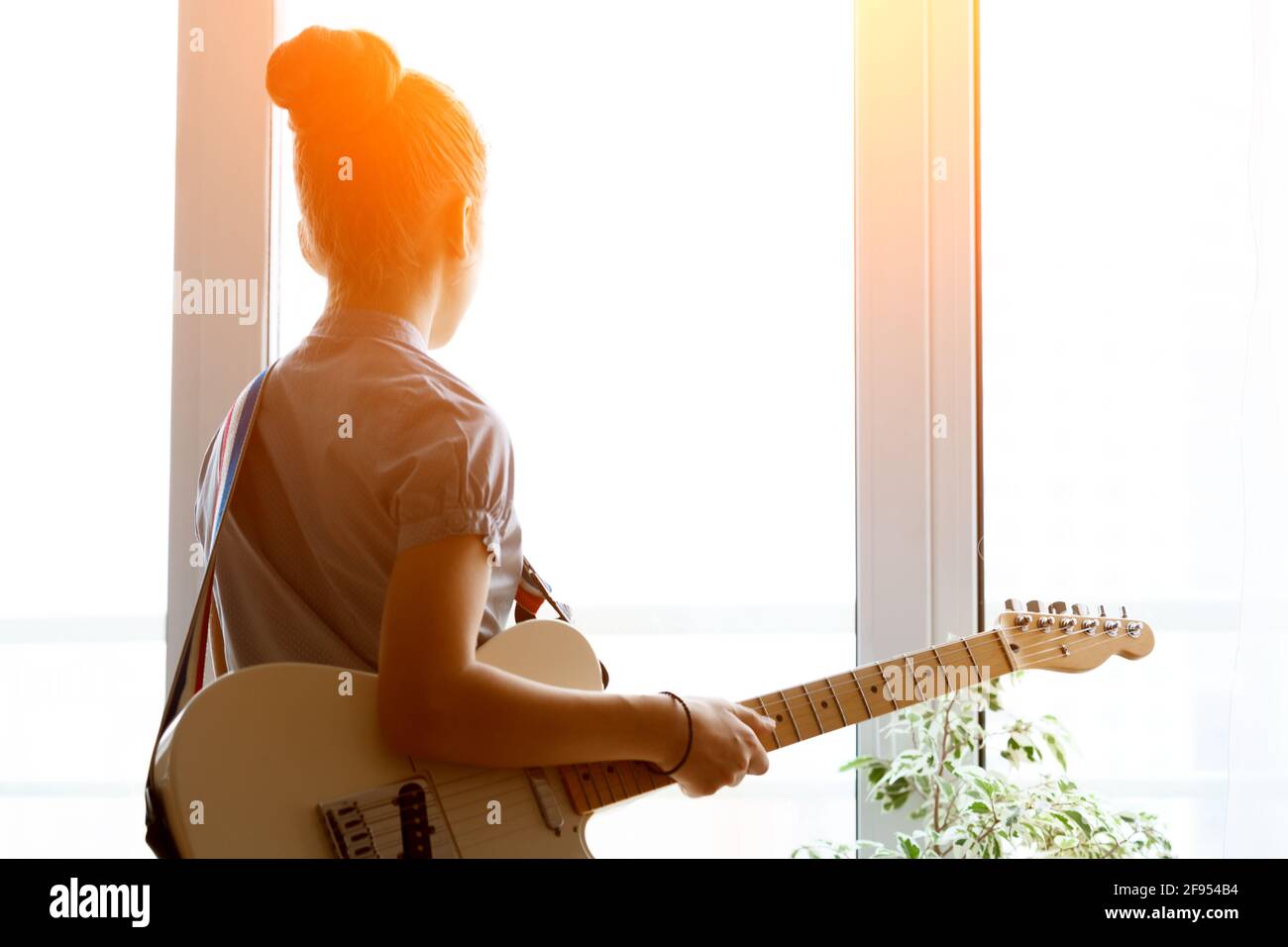 Silhouette di una bella giovane ragazza con una chitarra vicino alla finestra. Foto Stock