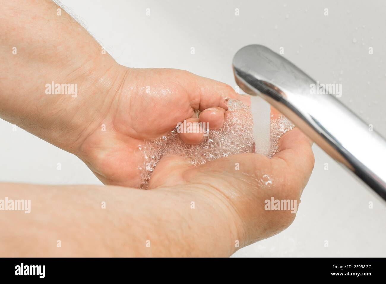 L'uomo anziano le lava le mani sotto il rubinetto in bagno, raccomandazione per frequenti lavaggi delle mani, igiene domestica. Foto Stock