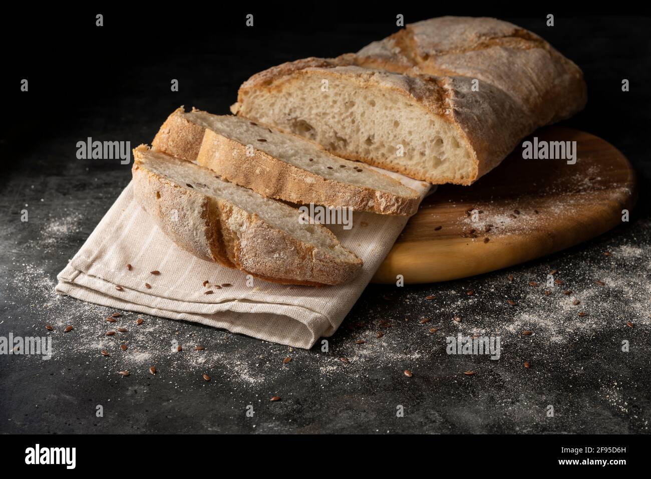 Le fette di pane bianco sono tagliate da una pagnotta più grande su un tagliere di legno e sfondo scuro Foto Stock