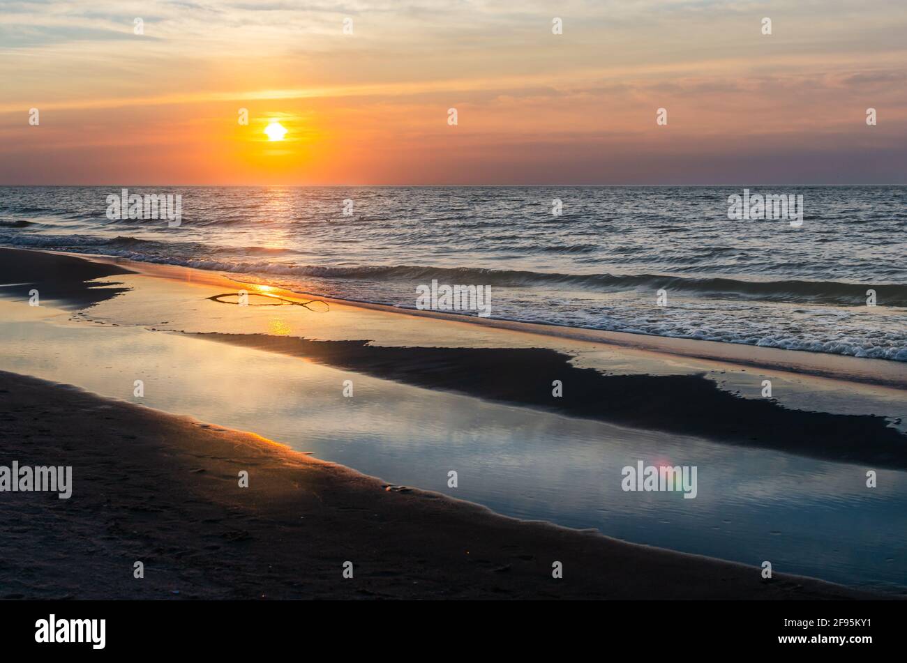 Tramonto sul Mar Baltico. Spiaggia di sabbia. I raggi del sole si riflettono nell'acqua. Foto Stock