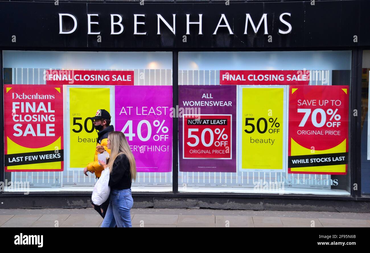 Un uomo e una donna passano davanti a un negozio Debenhams a Manchester, Greater Manchester, Inghilterra, Regno Unito, che mostra poster di "vendita di chiusura". Debenhams ha riaperto dozzine dei suoi negozi nel mese di aprile 2021 per una chiusura della vendita per la liquidazione delle scorte prima di una chiusura finale il 15 maggio. Il grande magazzino, crollato nel 2020, offre fino al 70% di sconto sulle sue scorte. Il Covid 19 o Coronavirus lockdown ha colpito mattoni e mortaio negozi duro. Foto Stock
