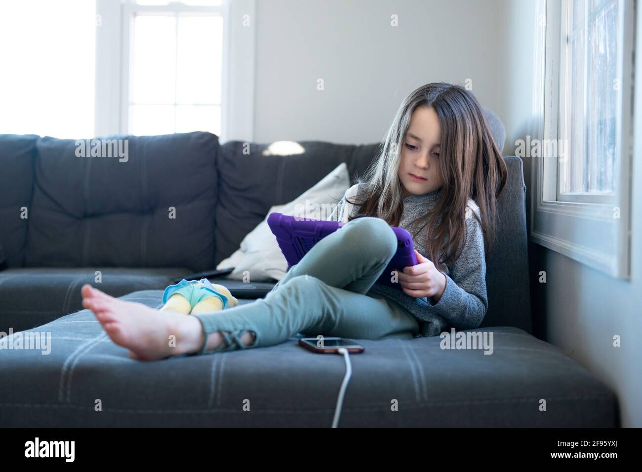 Bambina seduta sul divano con un tablet. Foto Stock