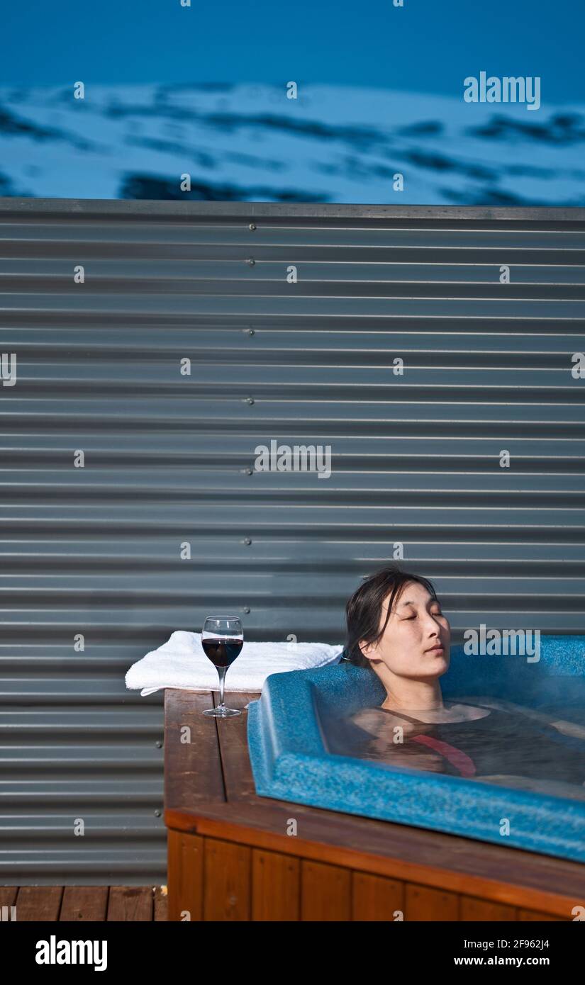 Donna che si rilassa nella vasca idromassaggio fuori dello chalet in Islanda Foto Stock