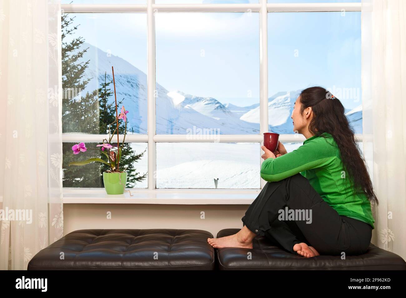 Donna che guarda fuori dalla finestra della casa vacanze islandese Foto Stock