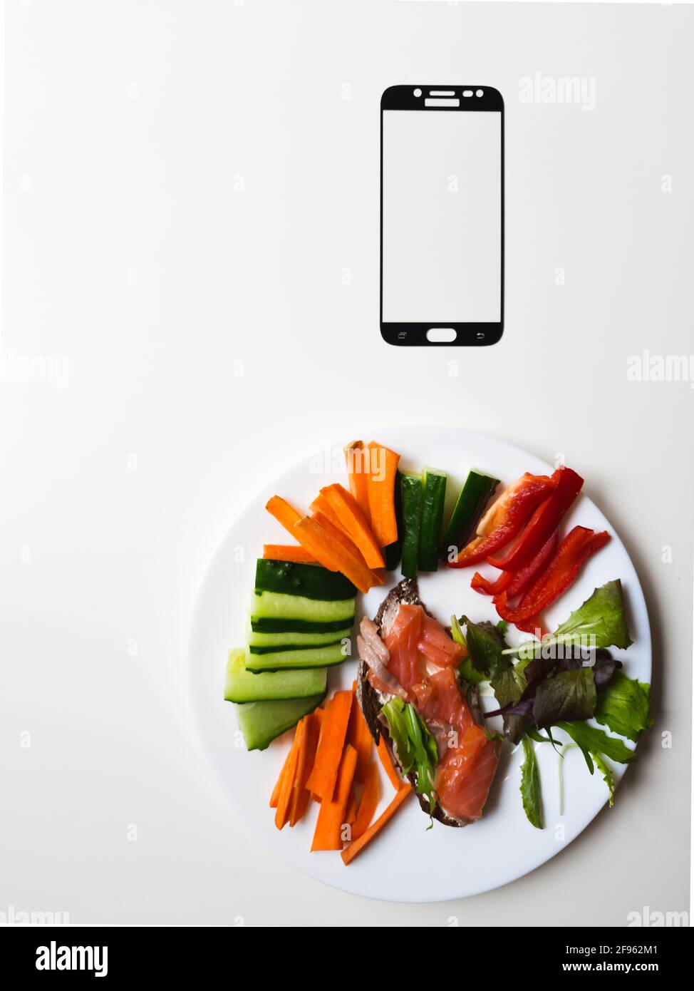 cornice per smartphone e piatto bianco con verdure e salmone tavola bianca Foto Stock