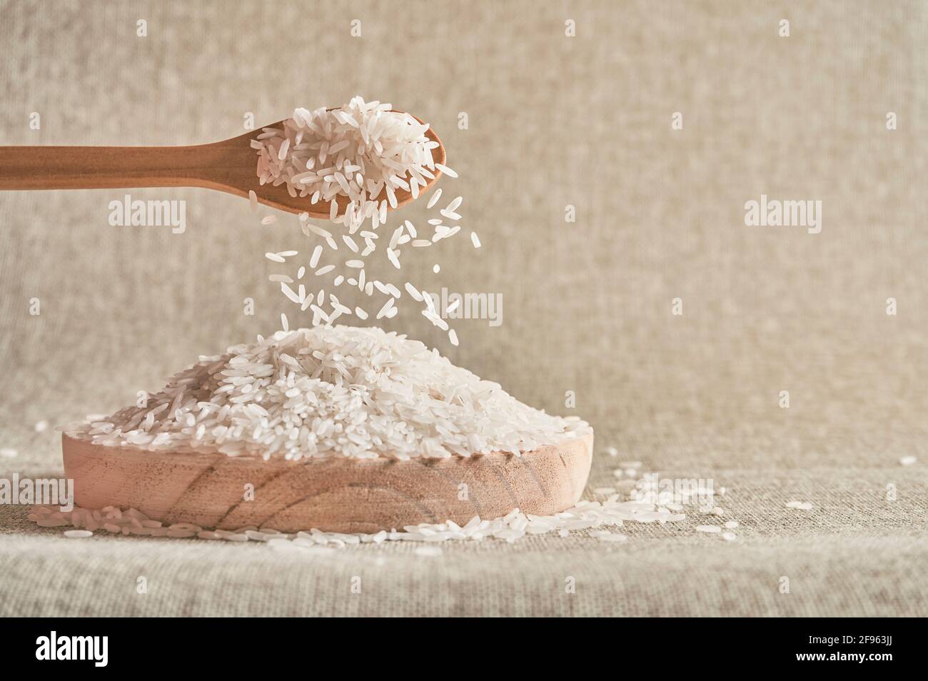 Primo piano di un cucchiaio di legno che versa riso bianco crudo su una piastra di legno Foto Stock