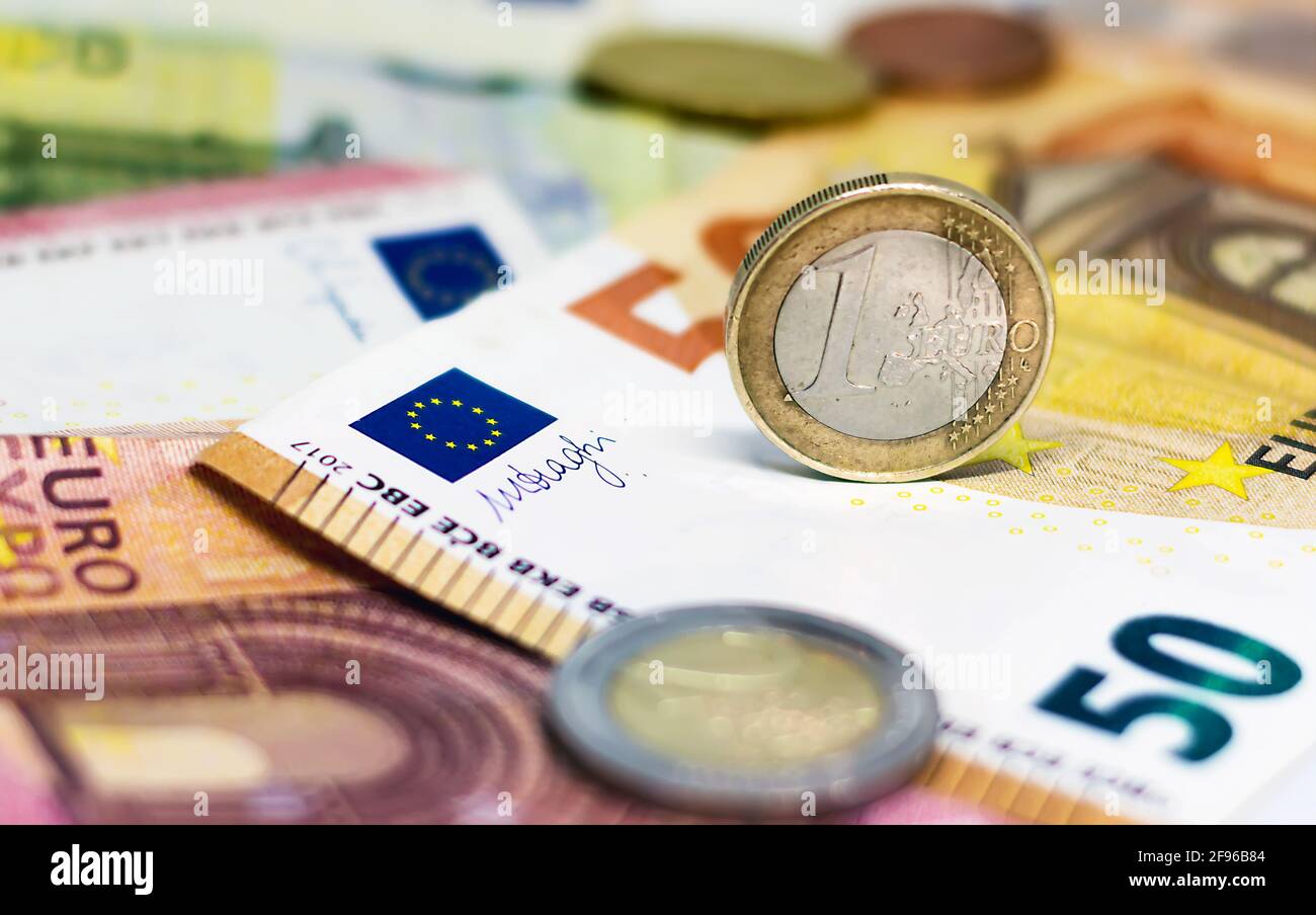 Una moneta da 1 euro usata in cima ad alcune banconote in euro. Economia e finanza nell'Unione europea. Foto Stock