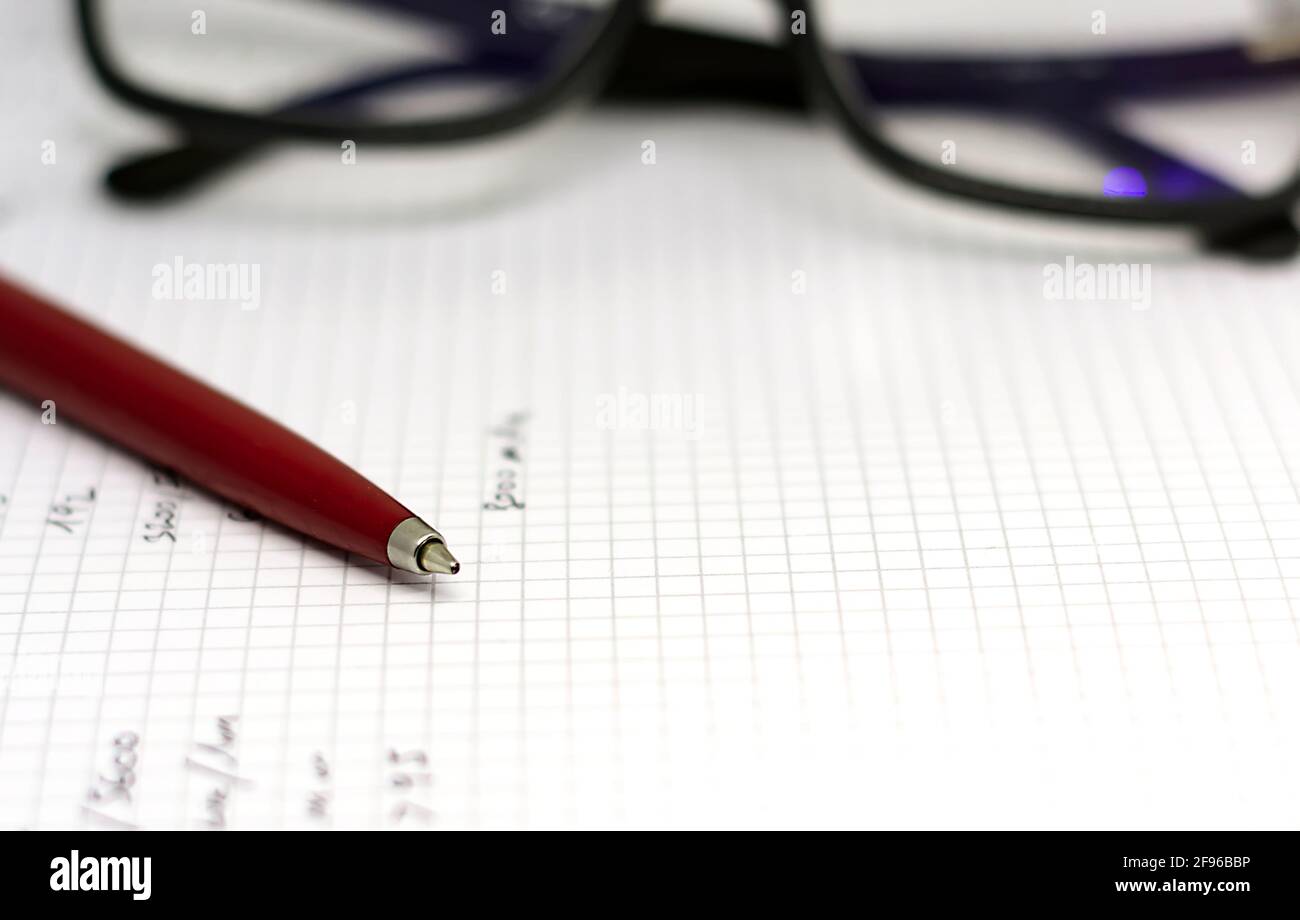 Penna a sfera rossa sulle pagine bianche di un taccuino aperto con un paio di occhiali sullo sfondo. Ispirazione e narrazione. Foto Stock