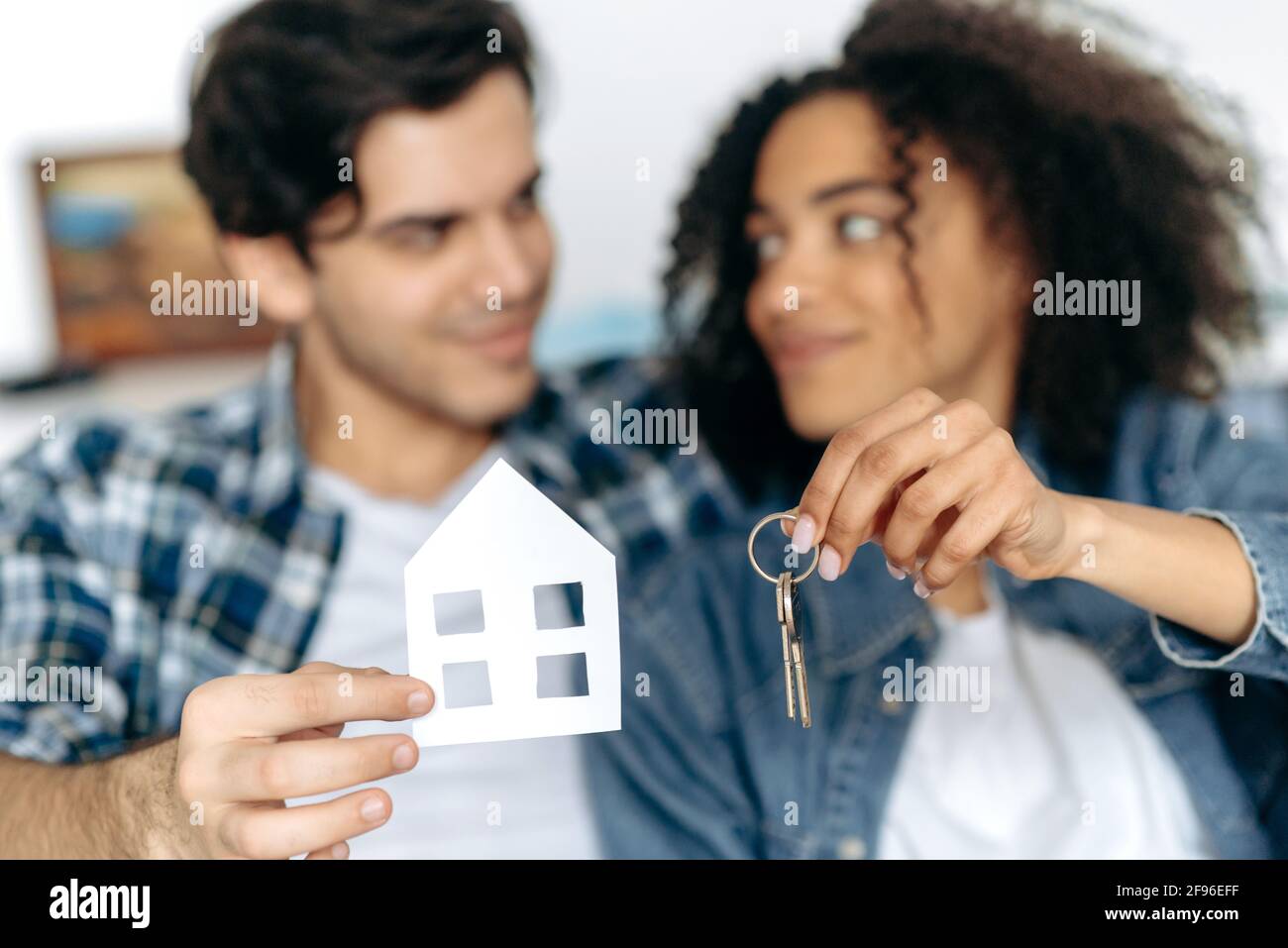 Acquisto di un nuovo alloggiamento. La felice coppia multirazziale affamata divenne il proprietario della loro prima casa, tenendo una piccola casa di carta e le chiavi per il nuovo appartamento, sorridendo, felice insieme Foto Stock