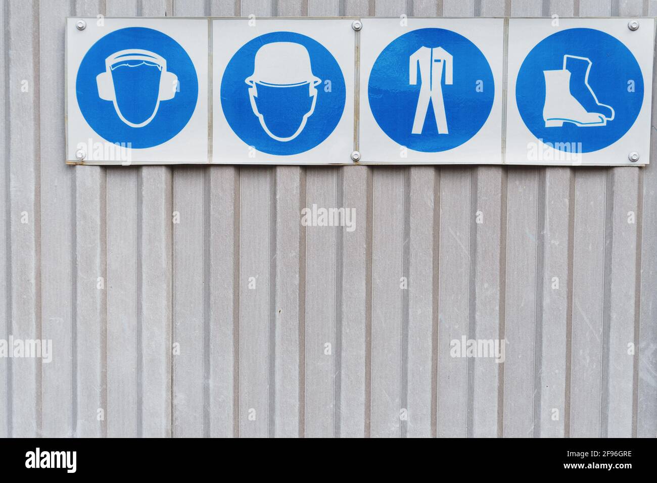 Cartelli e cartelli di sicurezza dei dispositivi di protezione individuale sul lavoro. Cuffie, casco, abbigliamento da lavoro, scarpe di sicurezza in fila Foto Stock