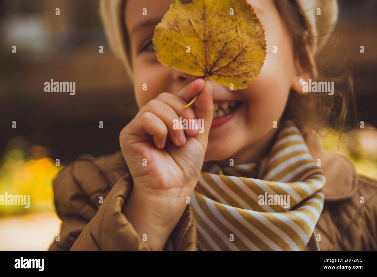 Una bambina tiene in mano una foglia gialla e nasconde il suo volto dietro di lui Foto Stock