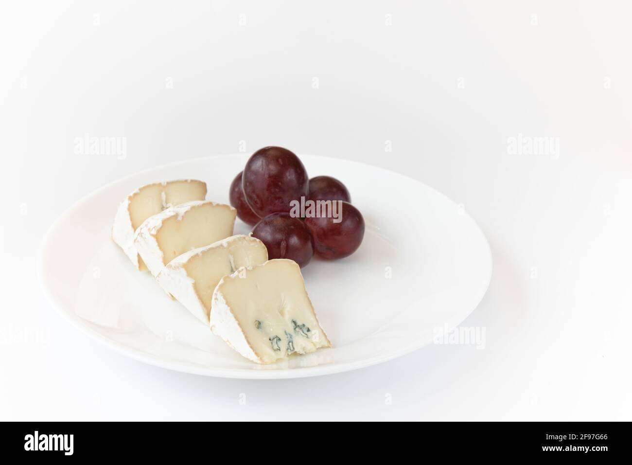 pezzi di camembert o di brie con uve rosse su piastra isolata su fondo bianco, formaggio morbido coperto di muffa bianca commestibile vista dall'alto, Foto Stock