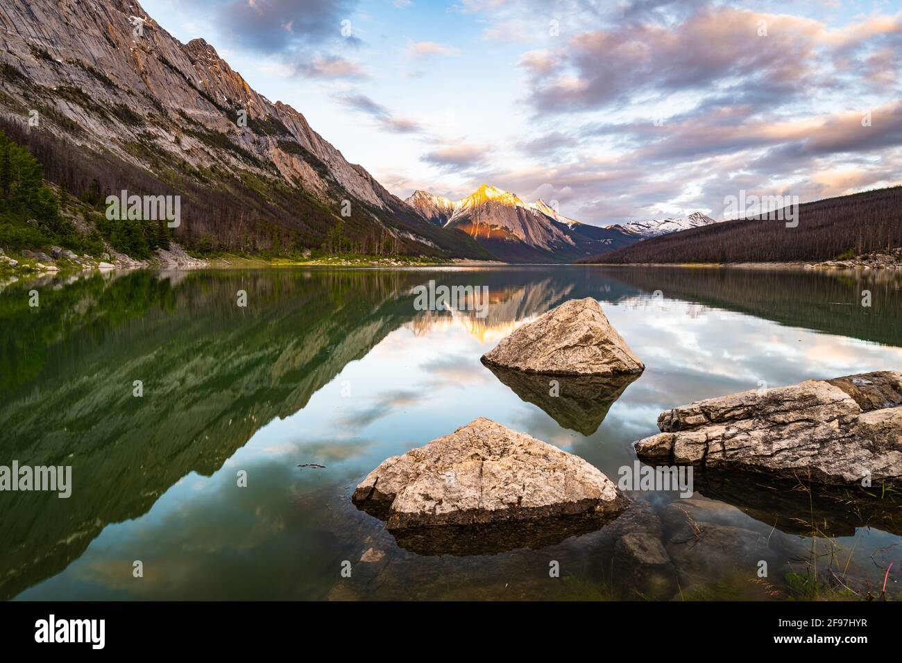 Una vista che guarda a sud attraverso il lago Medicine n Jasper National Parco con masso in acqua in primo piano e. cielo parzialmente nuvoloso sopra Foto Stock