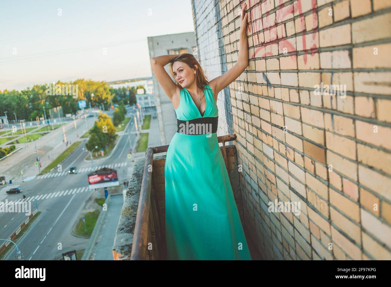 Attraente ragazza si pone in un abito verde menta sul balcone di un alto edificio. Foto Stock