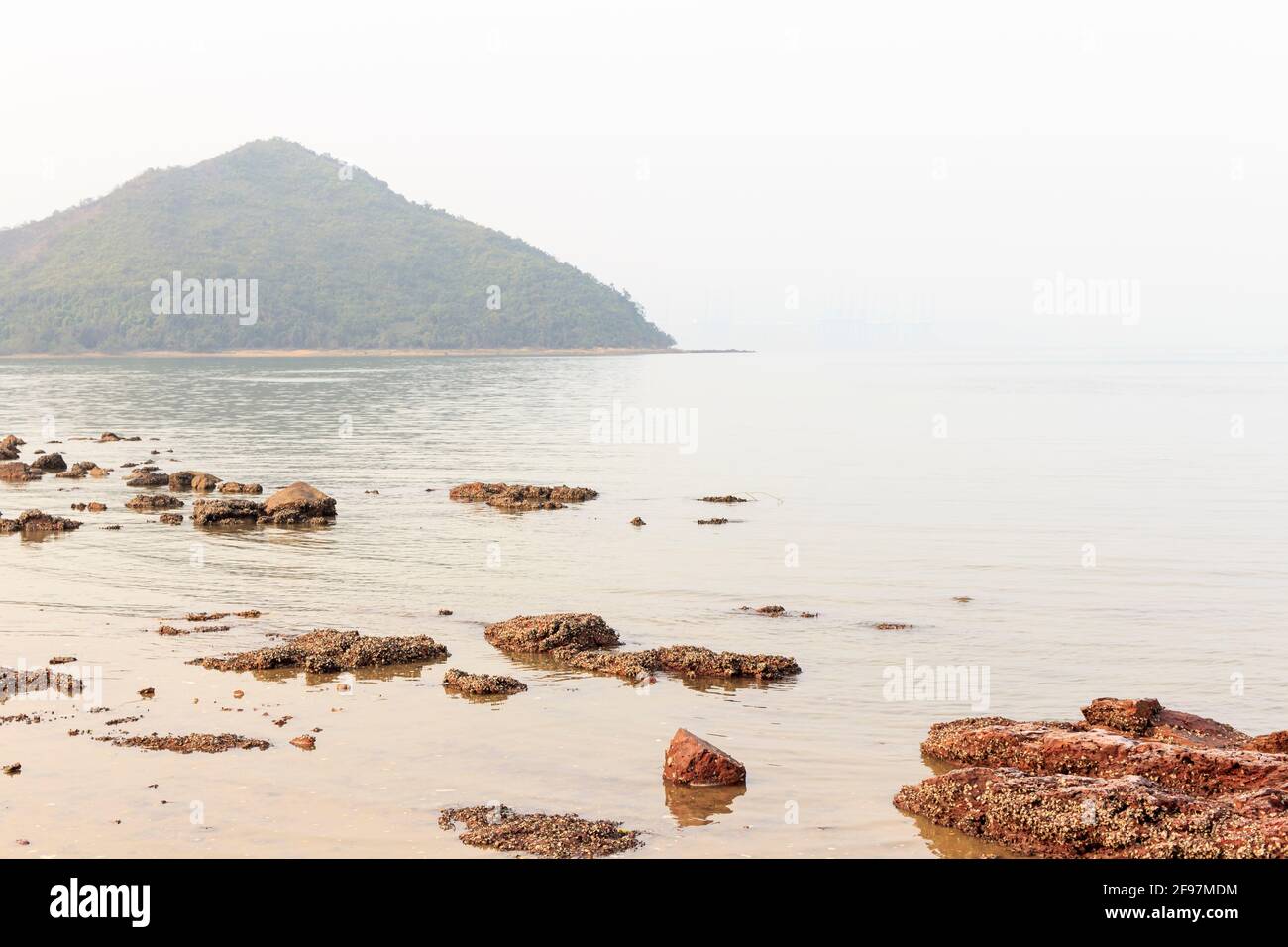 Bellissima vista mare con rocce di fronte e isola di montagna lontano. Foto Stock