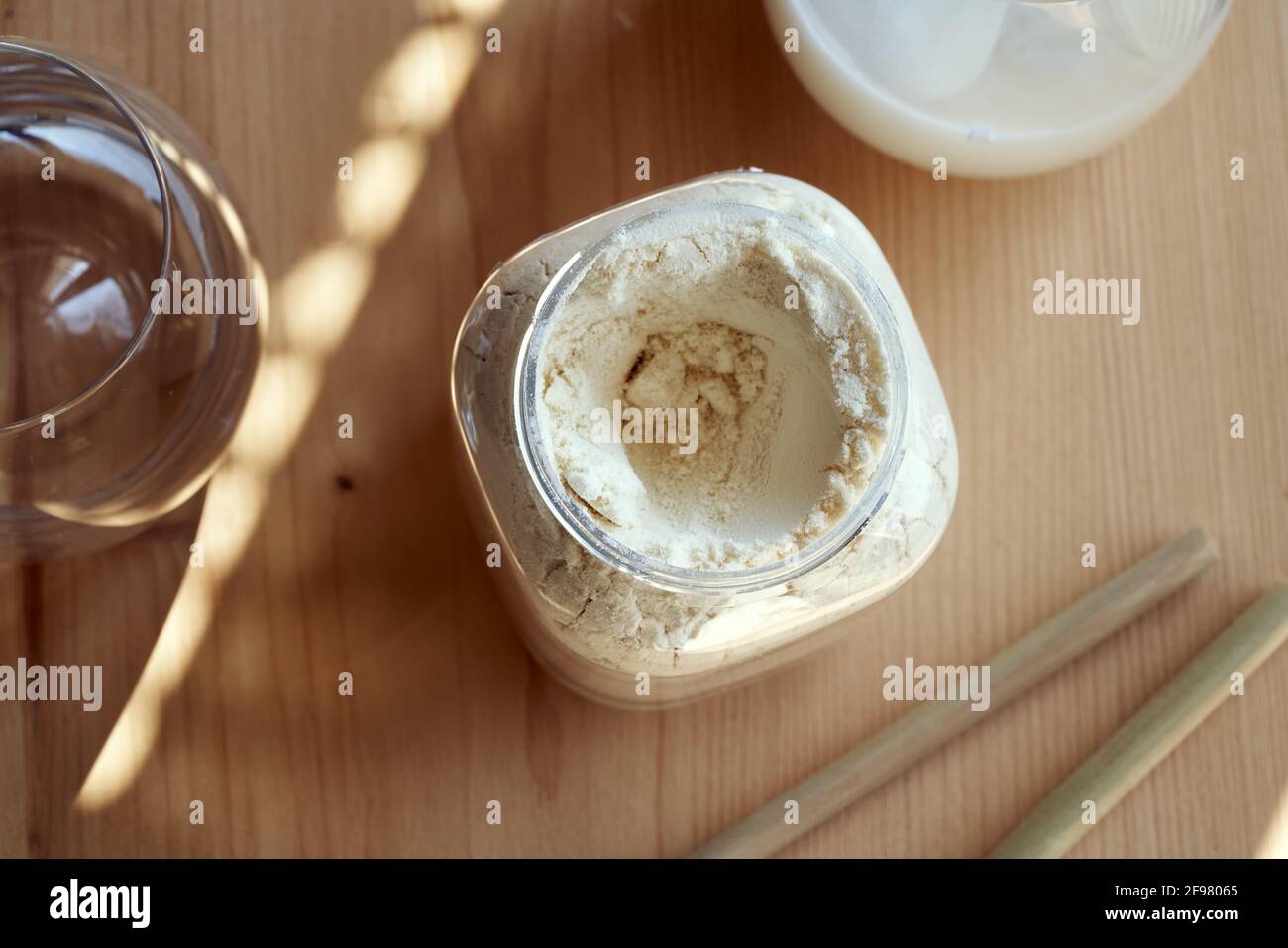 Polvere proteica di siero di latte in un vaso di plastica, con bevande e cannucce di bambù sullo sfondo Foto Stock