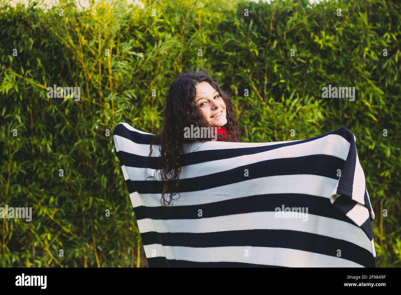 donna coperta con coperta a strisce in campo contro foglie di bambù Foto Stock