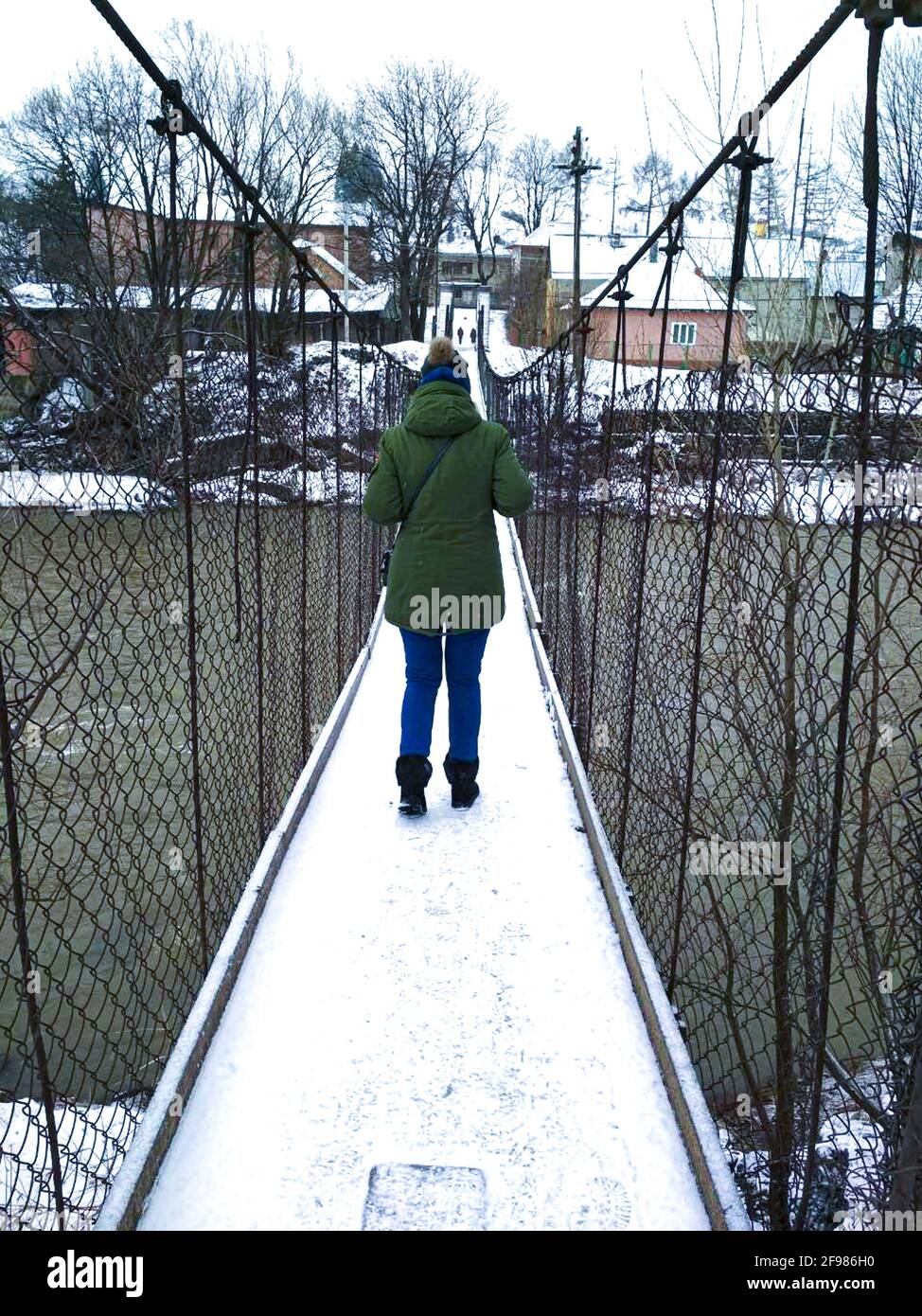 donna che cammina sul ponte sospeso sul fiume Foto Stock