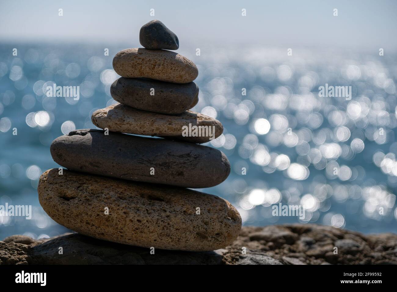 Equilibrata piramide di ciottoli sulla spiaggia in una giornata di sole. Abstract Sea bokeh sullo sfondo. Messa a fuoco selettiva. Pietre Zen sulla spiaggia di mare, meditazione Foto Stock