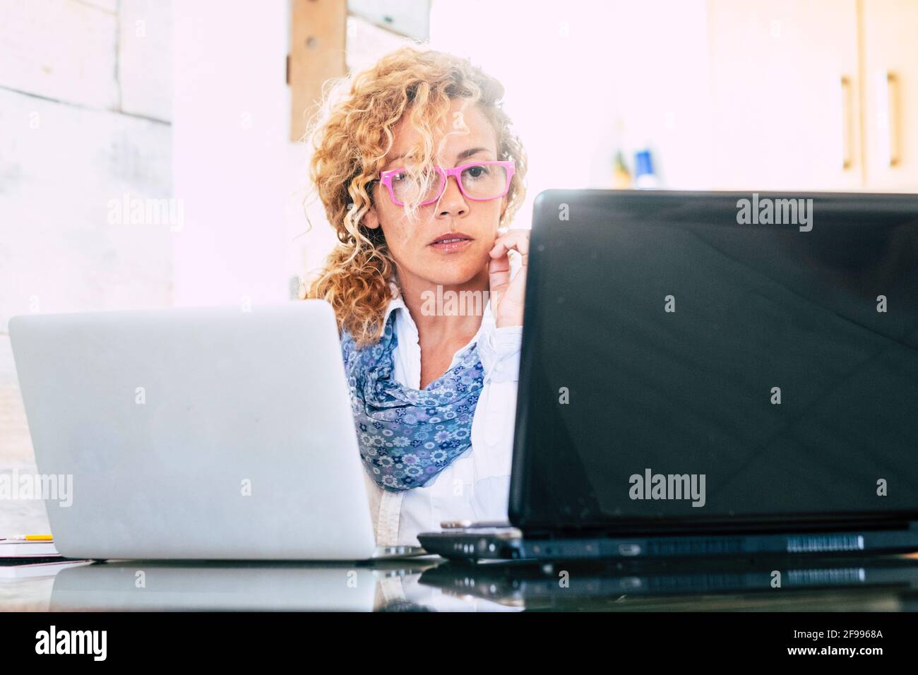 Casa ufficio lavoro donna caucasica persone con due computer portatile - uomini d'affari e di lavoro intelligenti persone di stile di vita - adulti guarda il display del pc e internet lavoro di formazione online Foto Stock