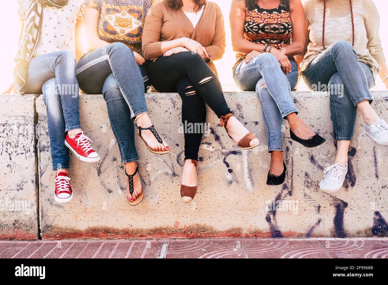 Gruppo di giovani donne irriconoscibili siedono insieme come un squadra su una parete di cemento in attività di svago all'aperto e. concetto di amicizia Foto Stock