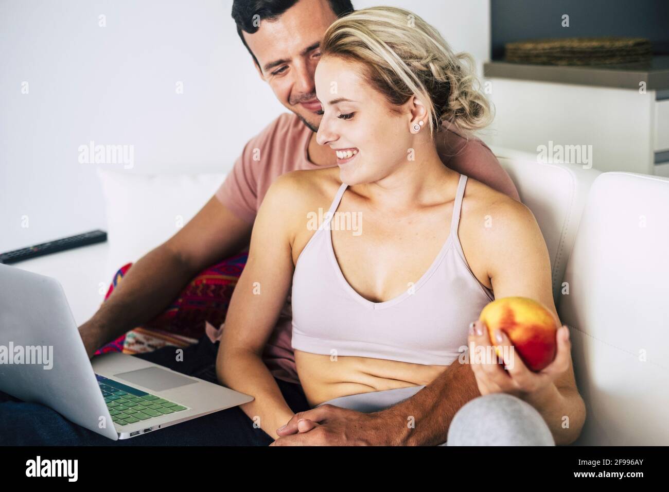 Stile di vita sano giovane coppia a casa godere di tecnologia e naturale cibo lavorando insieme su un computer portatile e mangiare una mela - persone in elazionship rfelice durante il blocco coronavirus Foto Stock
