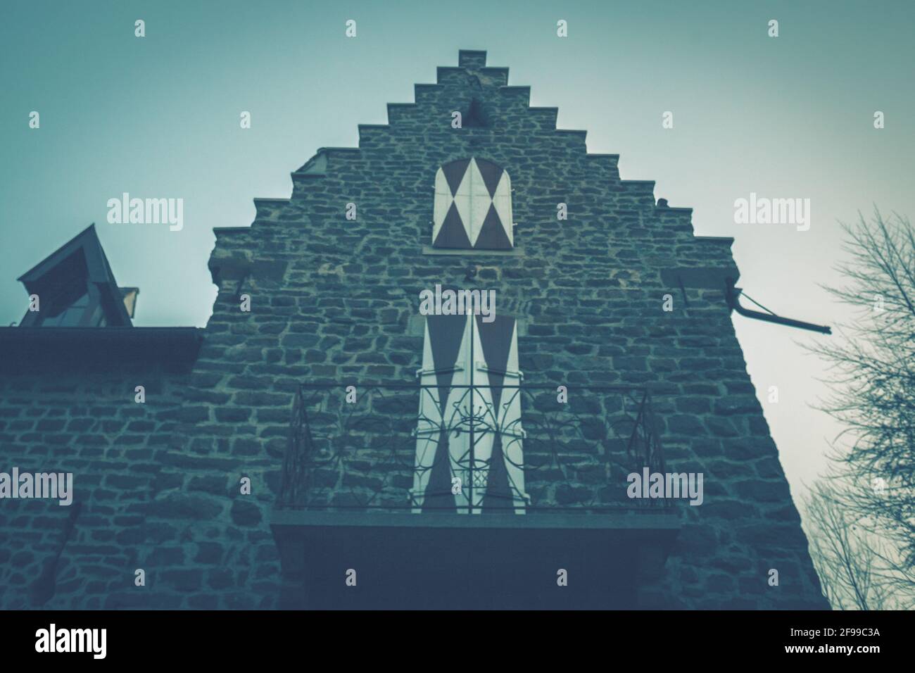 Una casa medievale con una torre, merli e finestre a bovindo e persiane chiuse. Malinconia, umore cupo Foto Stock