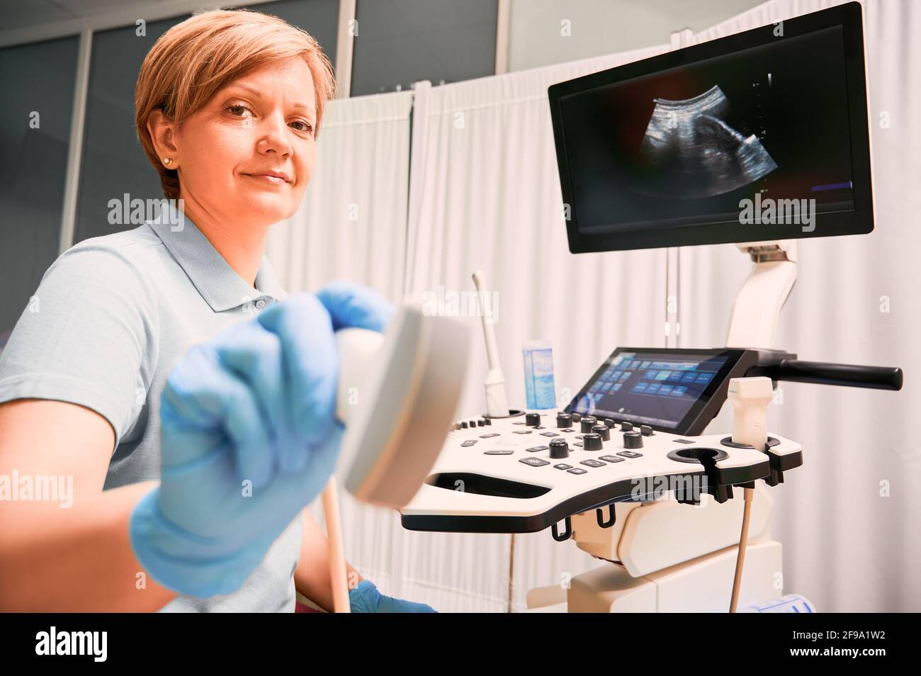 Donna in guanti sterili con trasduttore a ultrasuoni. Ecografo medico femminile che utilizza un moderno scanner a ultrasuoni in cabina ginecologica. Concetto di assistenza sanitaria e diagnostica ecografica. Foto Stock