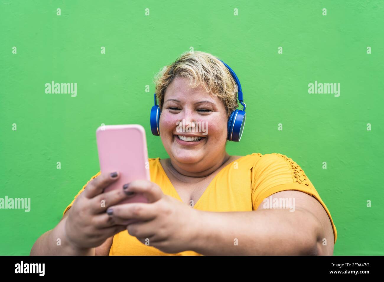 Donna di dimensioni Plus felice che prende selfie con smartphone mobile e. ascolto di musica con le cuffie wireless Foto Stock