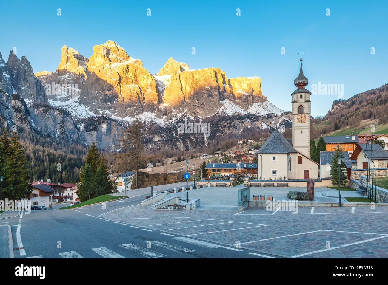 Colfosco, alta Badia, Dolomiti, Alto Adige, Italia. Il paese e la chiesa di San Vigilio con il gruppo del Sella sullo sfondo Foto Stock
